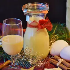 Szklanka i butelka z likierem jajecznym, jajka, cynamon i świąteczne ozdoby. Utrata aromatu przez otwarte likiery owocowe może być widoczna w ich wyglądzie.