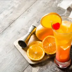 Kolorowy drink z pomarańczy i wiśni, obok pomarańcze i miarka barmańska. Czy sól na rancie szklanki faktycznie wzmacnia smak tequili?
