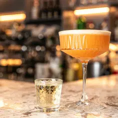 Domowe puree z marakui do Pornstar Martini. Koktajl w kieliszku coupe i shot z wódką na blacie barowym.
