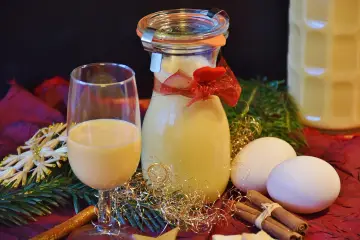 Szklanka i butelka z likierem jajecznym, jajka, cynamon i świąteczne ozdoby. Utrata aromatu przez otwarte likiery owocowe może być widoczna w ich wyglądzie.