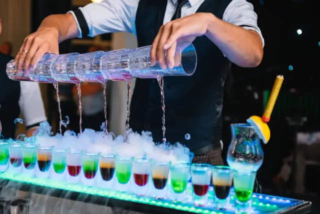 Barman przygotowuje autorskie drinki na powitanie gości na weselu. Kolorowe shoty z dymem tworzą magiczną atmosferę.