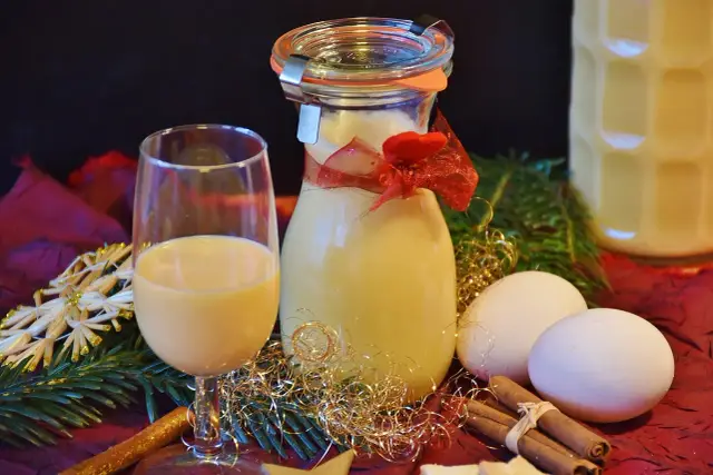 Szklanka i butelka z likierem jajecznym, jajka, cynamon i świąteczne ozdoby. Utrata aromatu przez otwarte likiery owocowe może być widoczna w ich wyglądzie.